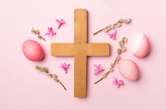 Pink Easter eggs with cross and palm leaves on color background, top view