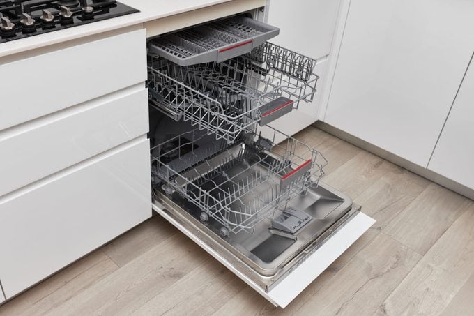 Modern built-in empty dishwasher with the door open showing three racks 