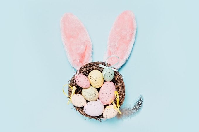 Easter Bunny Ears with Speckled Eggs in Nest on a pastel blue background.