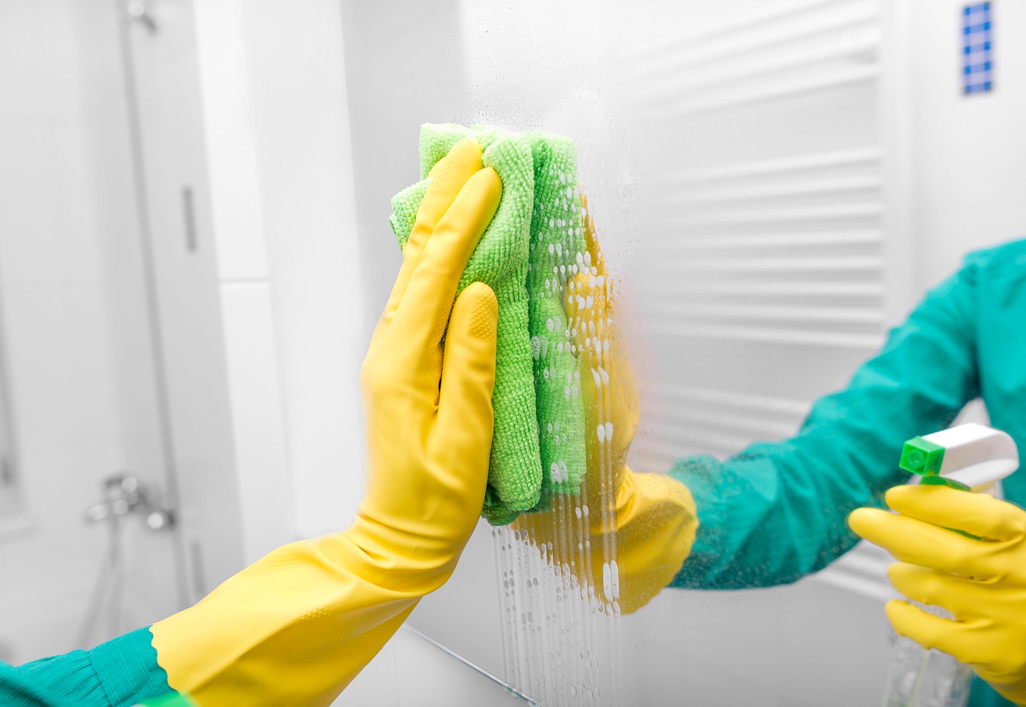 Hands in yellow gloves washing the mirror spray.