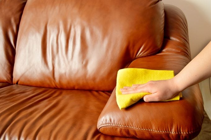 A person cleans a brown leather sofa.