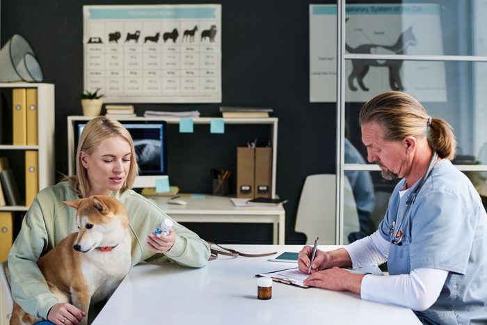 Female Dog Owner Talking To Male Veterinarian While He Writing Medical Prescription For Her Pet