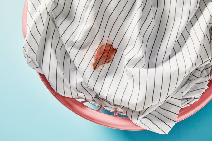 Sheets with a dried blood stain in a laundry basket on blue background