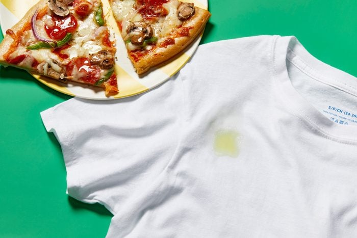 Oil and grease stain on white tshirt from pizza, shown nearby, on green background