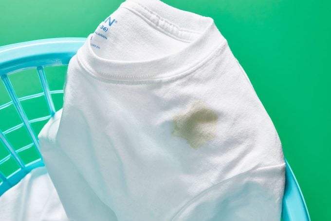 white tshirt with old oil stain in a laundry basket, green background
