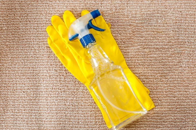 yellow rubber gloves and a clear spray bottle with ammonia on a carpet for cleaning stains