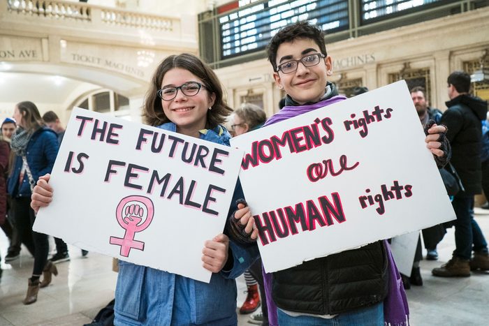 two young people holding signs. One says "the future is female." the other sign says "women's rights are human rights"