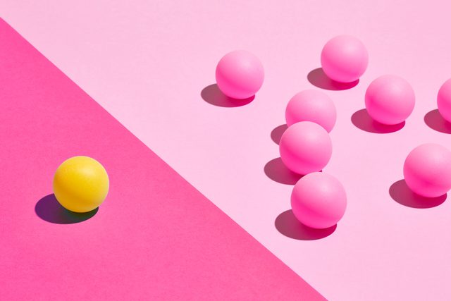 one yellow ball on the left on a dark pink background and multiple pink balls on the left on a lighter pink background with a clear line between the two sides