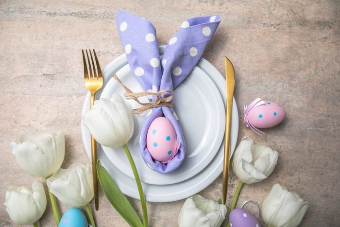 Easter holiday table setting with bunny from egg on white plate and tulips flowers. Gray concrete table, top view with copy space for text. Happy Easter background