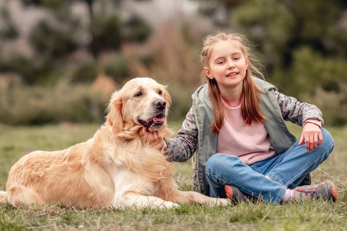 Little beautiful girl sitting on the grass with golden retriever dog outside