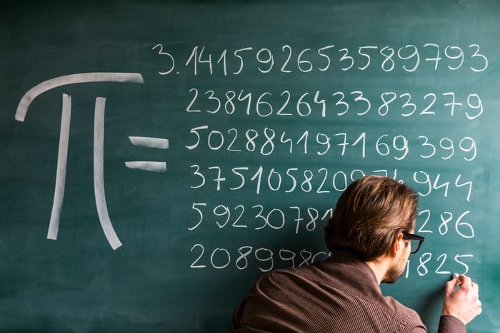 Teacher, student, scientist hand writing Pi numbers on green chalkboard