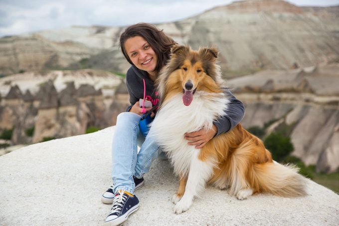 Young happy girl sitting with collie dog in Cappadocia valley 