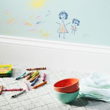 crayon drawing on a light blue wall with crayons, bowls, and cleaning cloths on the floor