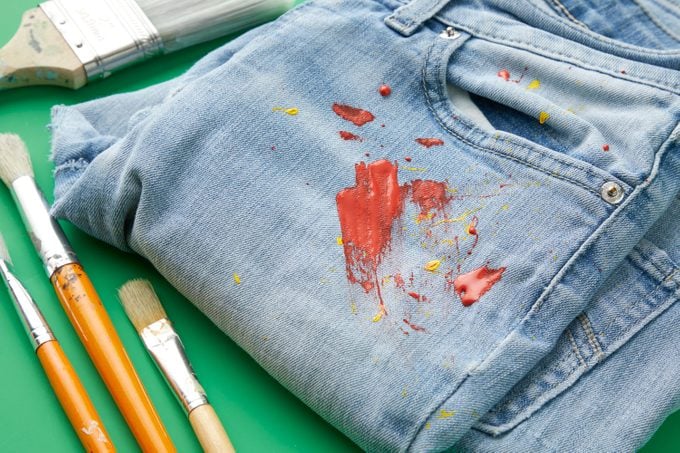 Close up of paint stain on denim jeans with paintbrushes nearby