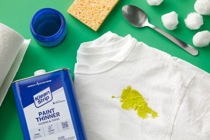 Greenish oil-based stain on a white t-shirt on green background with supplies to clean the stain surrounding