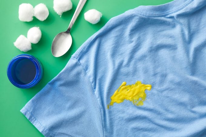 Yellow acrylic, water-based paint stain on a blue t-shirt on green background with supplies needed to clean it nearby