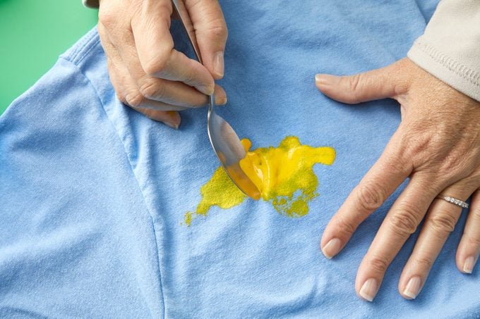 Hands removing excess paint from the t-shirt with a spoon