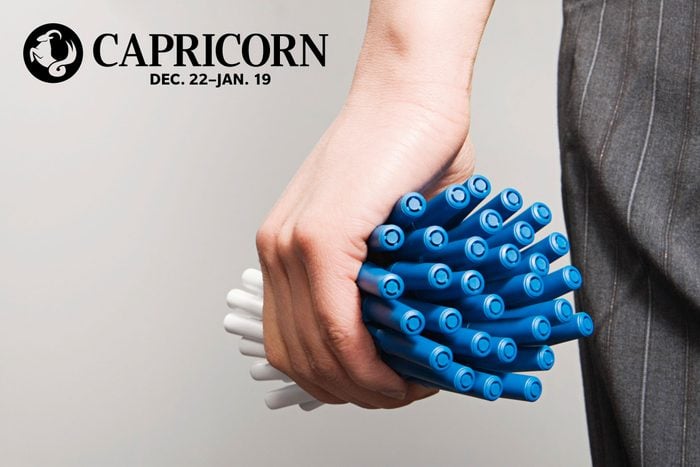 hand holding a bunch of pens with capricorn zodiac in upper left corner