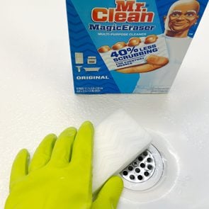 Hand with green glove cleaning a shower with mr clean magic eraser with a box in the background