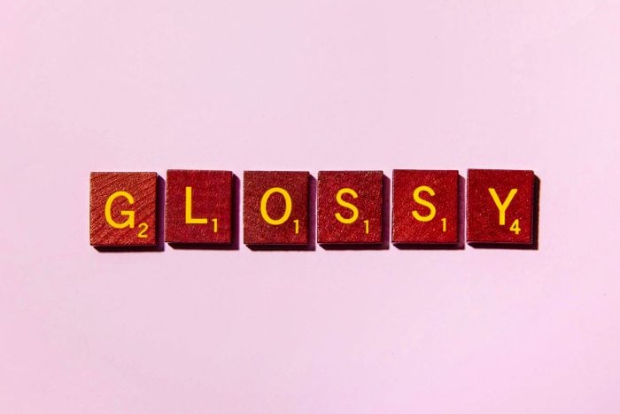 word GLOSSY in scrabble tiles on pink background