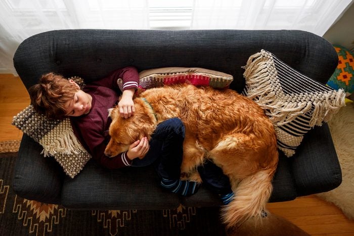 Boy lying on a couch cuddling a golden retriever dog