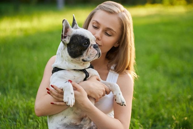 Woman holding purebred french bulldog in park.