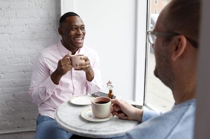 Man sitting at cafe table with a cup of coffee, smiling at another man