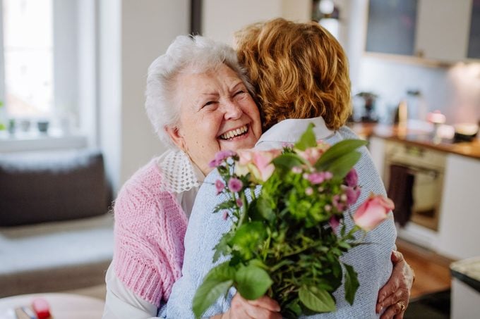 adult daughter hugging elderly mother and giving flowers on mother's day