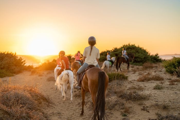 group of young riders on horseback heading towards the beach