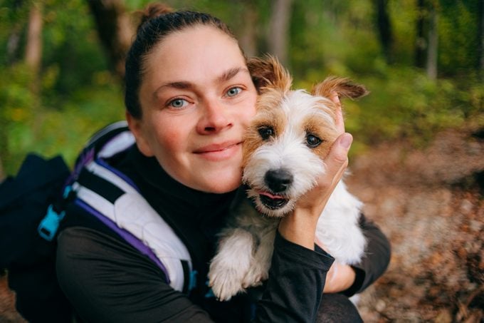 Middle aged woman hugs her dog during a forest walk. Jack Russell terrier.