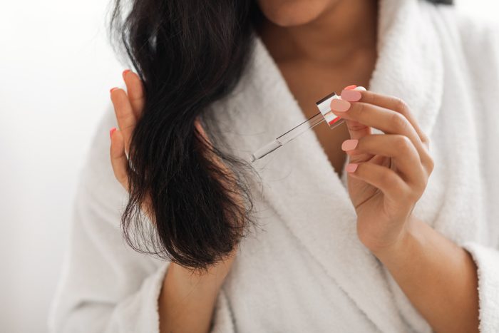 African American Woman Applying Serum On Hair Indoors, Cropped