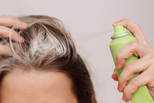 Close up of a young woman's head with dirty greasy hair. The girl spraying dry shampoo on the roots of her hair