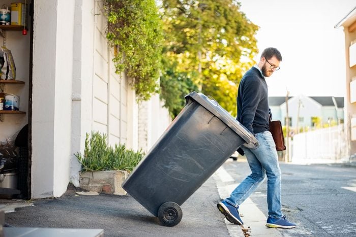 Man Pulling A Wheeled Dumpster Out Of His Garage While Going To Work