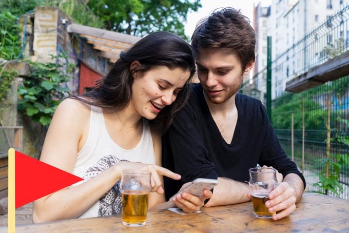 woman sitting close to a man on a date showing him something on her phone with a red flag icon in he bottom left corner